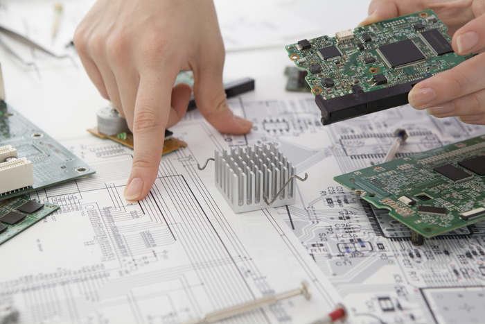 Technische Entwicklung: Von der Schaltung zum fertigen System Hand zeigt auf Schaltplan, umgeben von Leiterplatten und Kühlkörpern – technische Entwicklung von Embedded Systemen