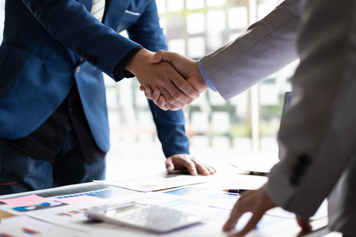 Vertrauensvolle Partnerschaft und gemeinsame Ziele Zwei Geschäftspartner beim Handschlag über einem Tisch mit Vertragsunterlagen – Symbol für Vertrauen und langfristige Zusammenarbeit